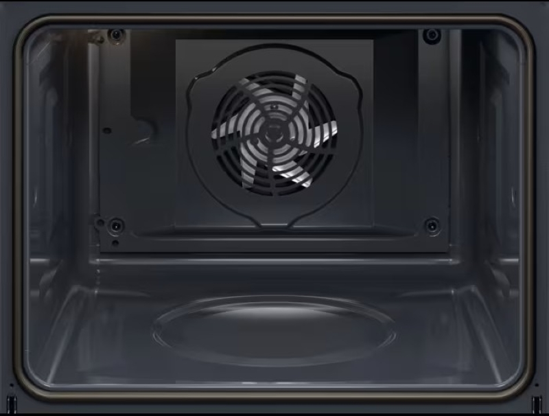Wnętrze ciemnego piekarnika. Wentylator jest wyśrodkowany z tyłu. Ściany piekarnika są ciemne i gładkie. Widoczna jest rama drzwi.