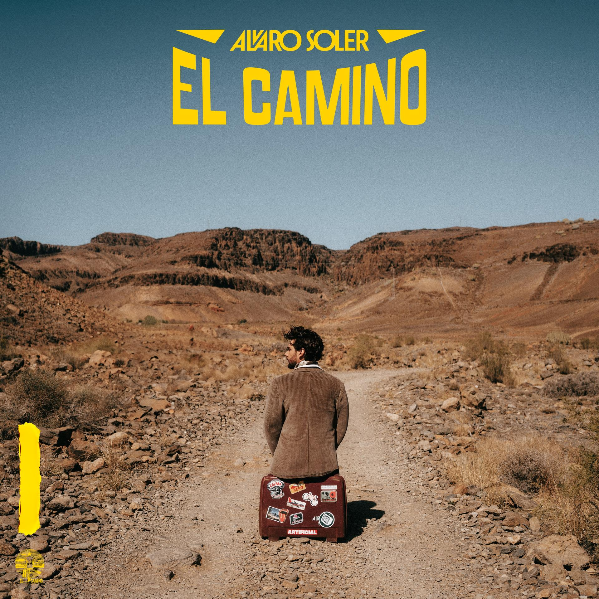Mann mit Gepäck steht auf einem Wüstenpfad. Der Text 'EL CAMINO' steht darüber. Im Hintergrund ein Gebirge, klarer Himmel.