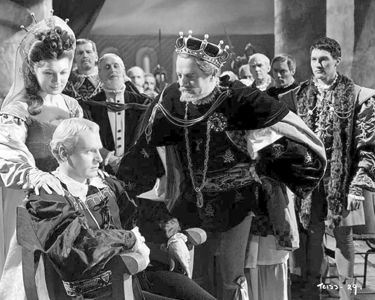 Ein König mit Krone, mit Gefolge, betrachtet einen sitzenden Mann. Eine Frau mit Haube steht daneben. Eine historische Szene.