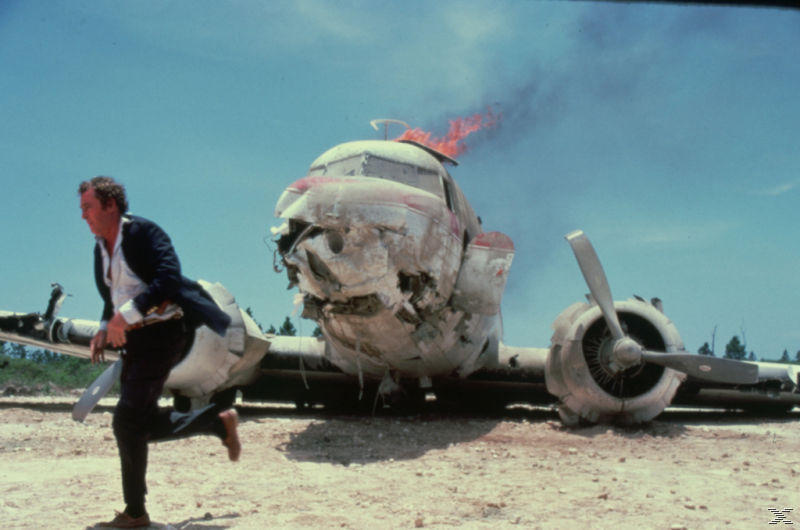 Ein abgestürztes Flugzeug mit Flammen und Rauch, ein Mann rennt weg vom Wrack unter klarem Himmel.