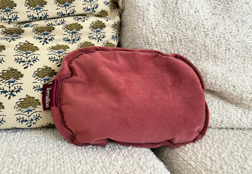 Un coussin bordeaux sur un canapé crème texturé. Un coussin à motifs avec un design floral est derrière le coussin bordeaux.