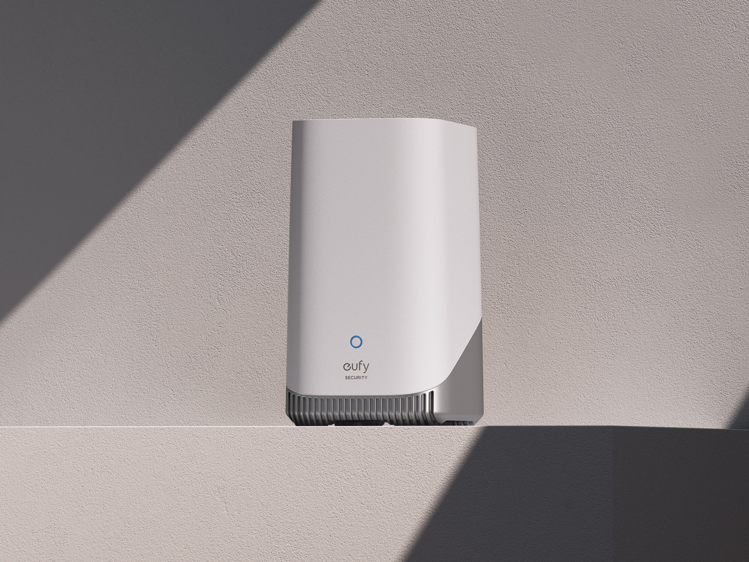Un dispositivo de seguridad eufy blanco y plateado está sobre un estante. El dispositivo tiene un círculo azul y el logo eufy.