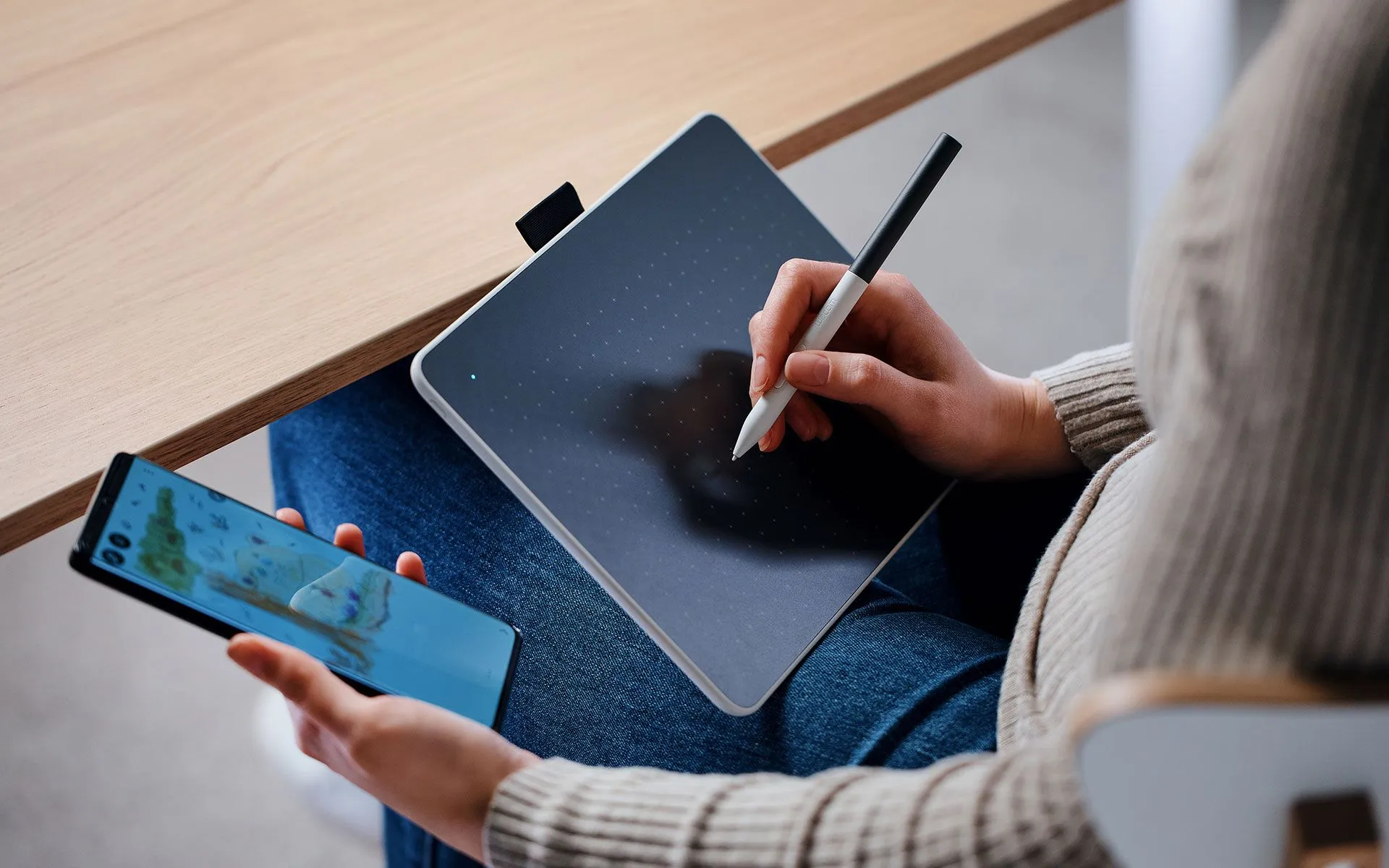Une personne utilise une tablette et un smartphone. La tablette est sur ses genoux et utilise un stylet.