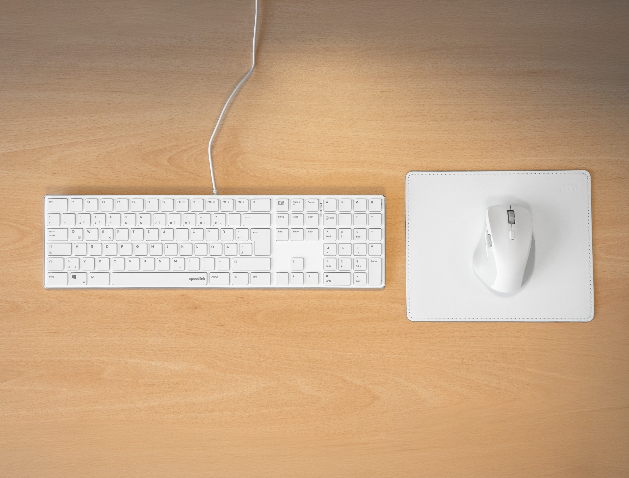 Weiße Tastatur, Maus und Mauspad auf einem Holztisch. Die Tastatur hat Tasten, die Maus rechts.