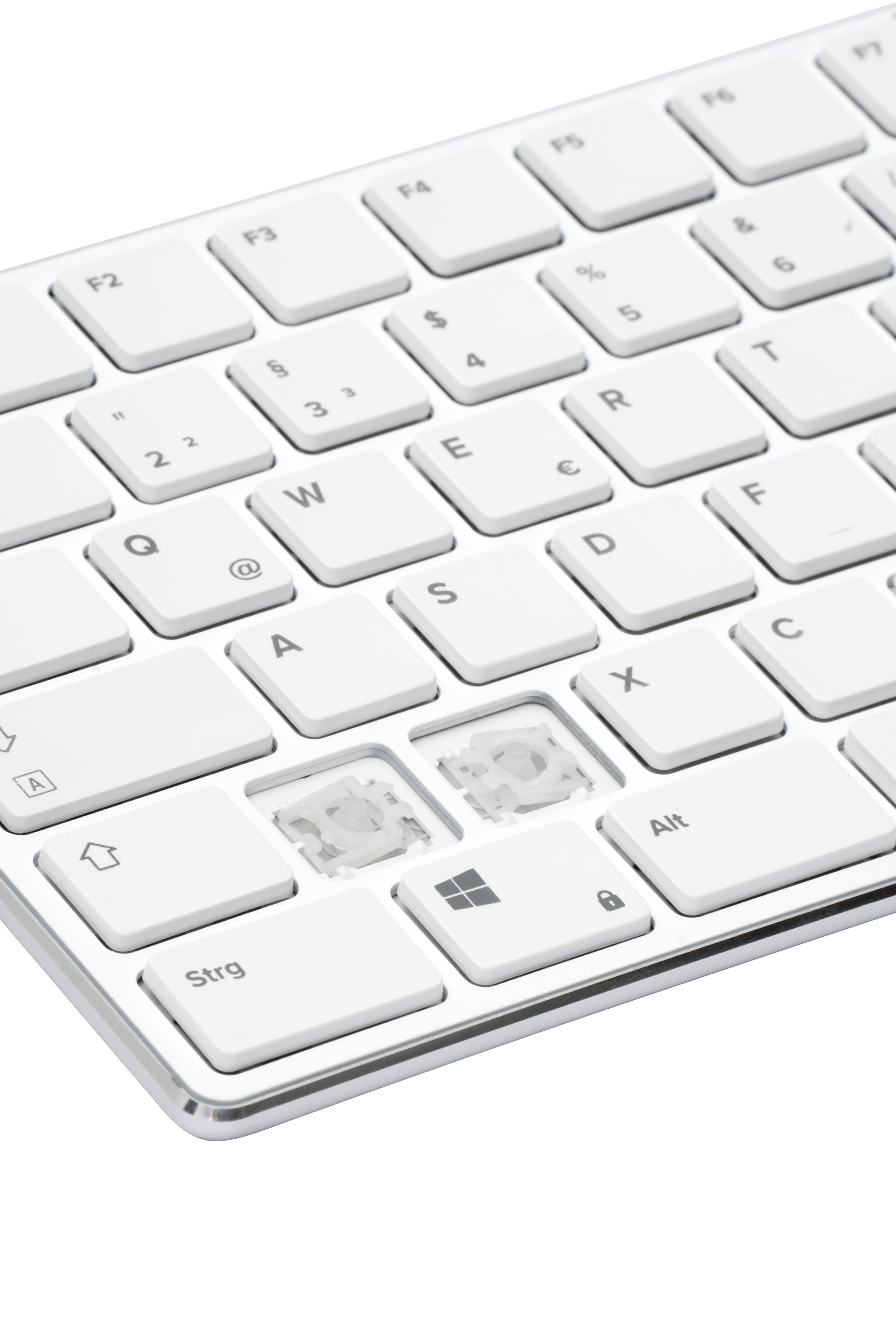 Nahaufnahme einer weißen Tastatur. Mehrere Tasten fehlen. Die Tasten tragen Buchstaben und Zahlen. Die Tastatur liegt auf weißem Untergrund.