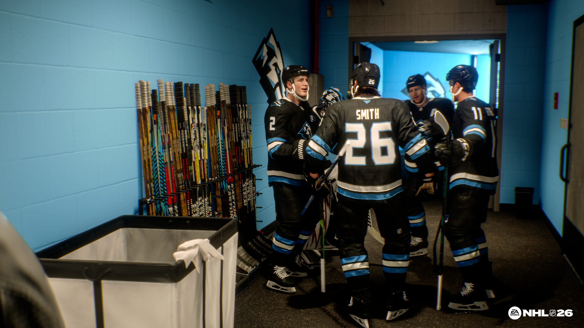 Eishockeyspieler in schwarzen Trikots mit blauen Akzenten versammeln sich in einer Umkleidekabine. Hockeyschläger säumen die Wand. Im Vordergrund steht ein Wäschekorb.