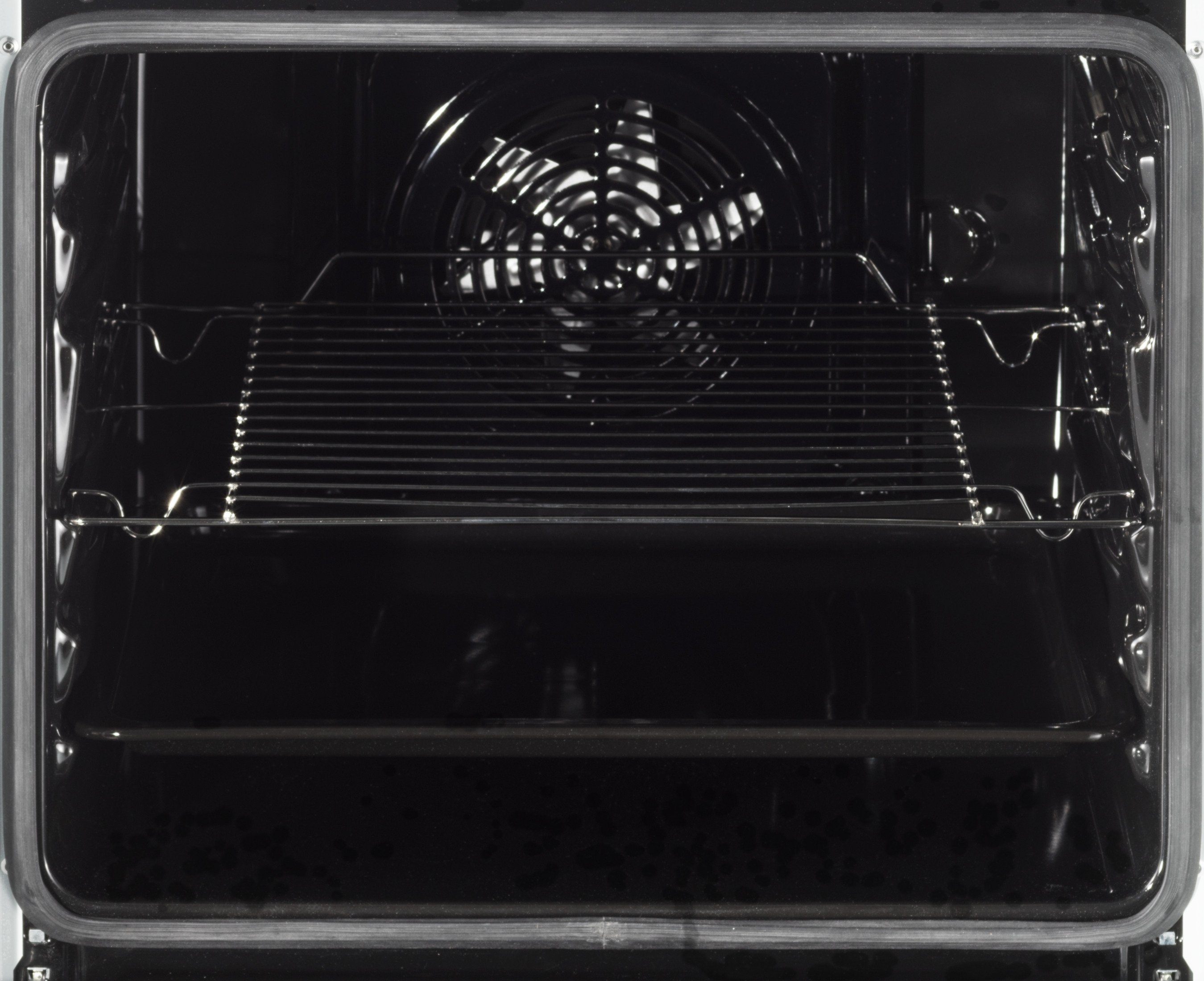 Pusty wnętrze piekarnika z wentylatorem, rusztami i ciemną, odbijającą powierzchnią.