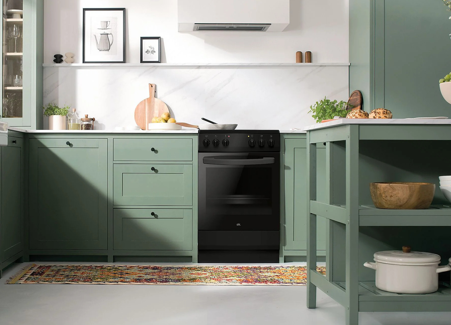 Nowoczesna kuchnia z zielonymi szafkami, czarnym piekarnikiem i kolorowym dywanem. Na ścianie wiszą obrazy i drewniana deska do krojenia.