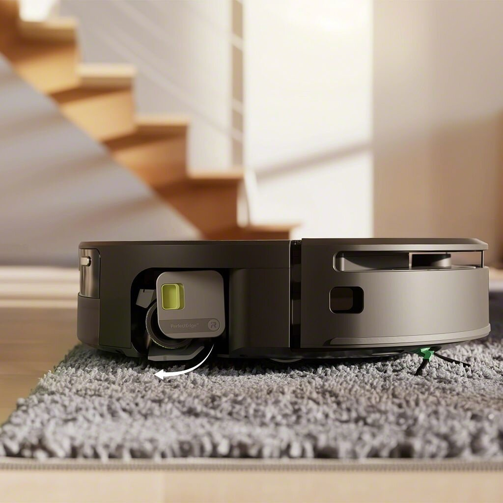 Szary robot odkurzający na szarym dywanie. Schody w tle. Odkurzacz ma zielony i szary element.