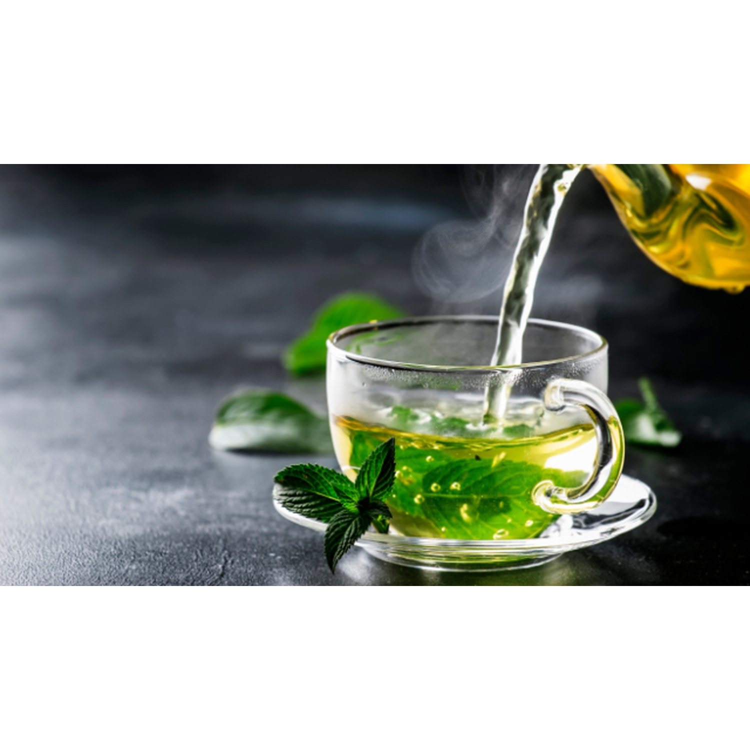 Una tazza di vetro trasparente con foglie di menta, piena di tè verde, vapore che sale. Tè versato da una teiera dorata. Sfondo grigio scuro.