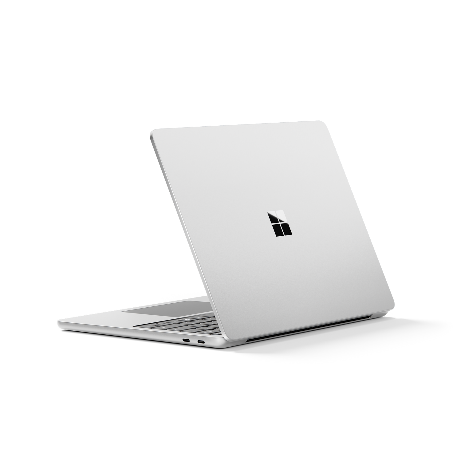 Un portátil plateado está ligeramente abierto sobre una superficie gris. El logotipo de Microsoft es visible en la tapa cerrada. El fondo es gris.