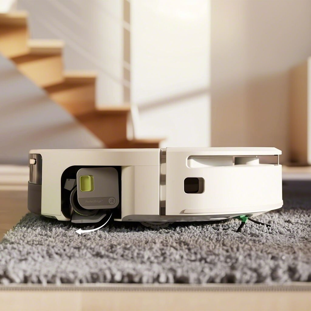 Robot odkurzający na szarej macie. Jest biały z szarą podstawą. W tle drewniane schody.