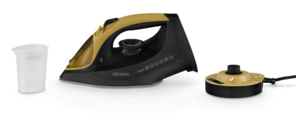 Żelazko Zeegma w czarno-złotym designie, miarka i stacja ładująca na białej powierzchni.
