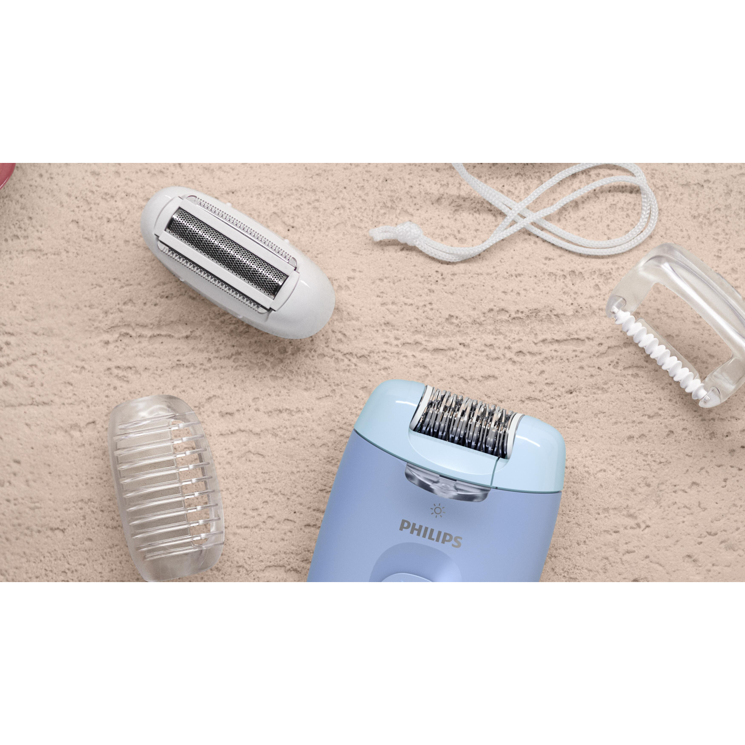 Vogelvlucht. Een Philips epilator, met opzetstukken, op een beige oppervlak. Onderdelen zijn wit en lichtblauw.