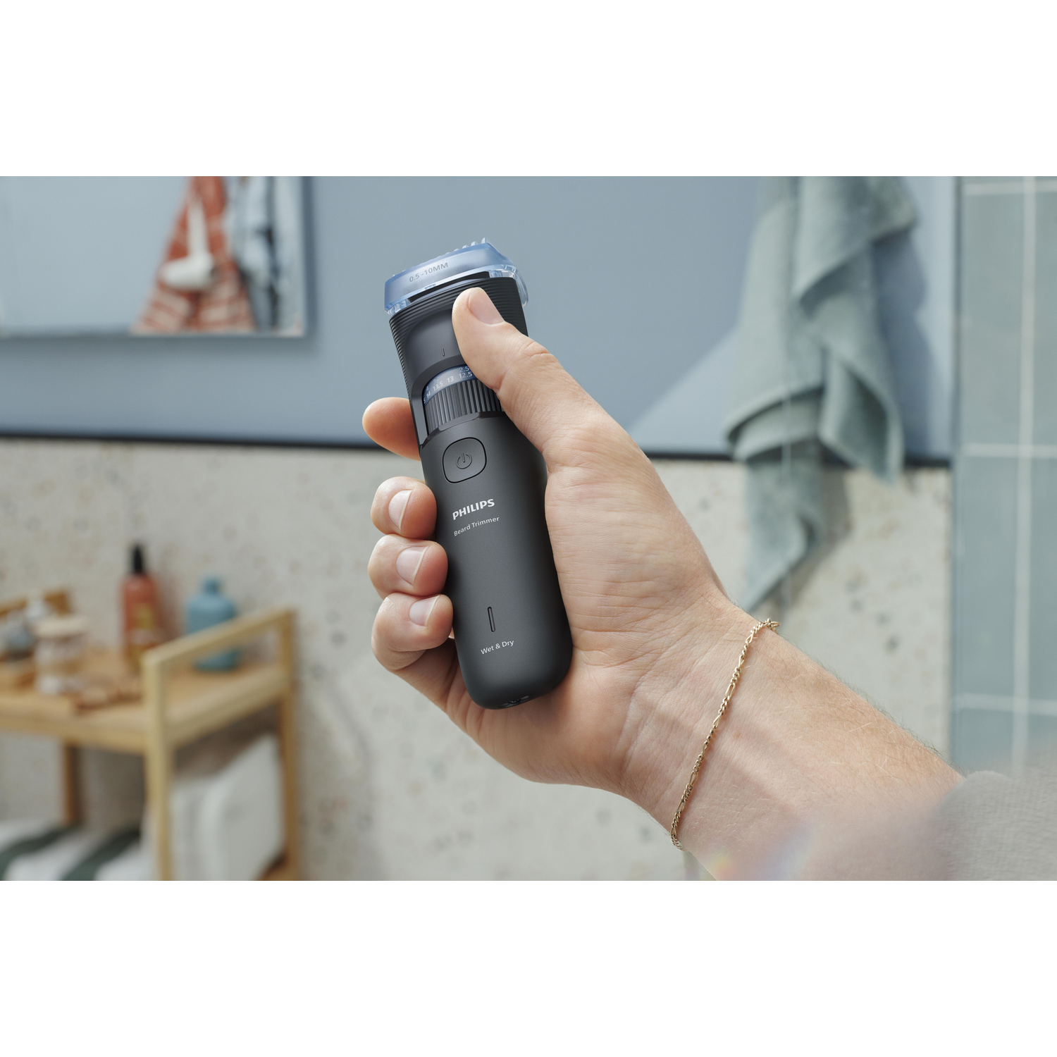 A hand holding a black Philips beard trimmer in a bathroom setting. A mirror and a towel are in the background.