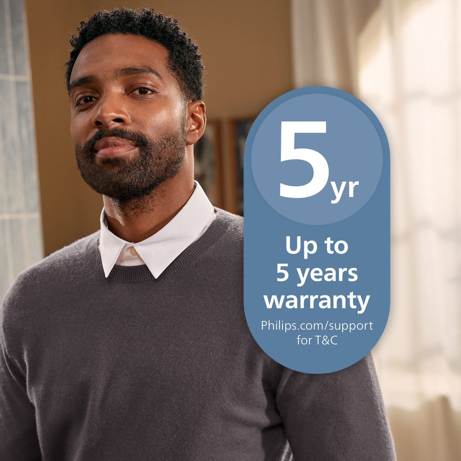 A man in a gray sweater and white shirt, with a 5-year warranty badge. The background is blurred, with a window.