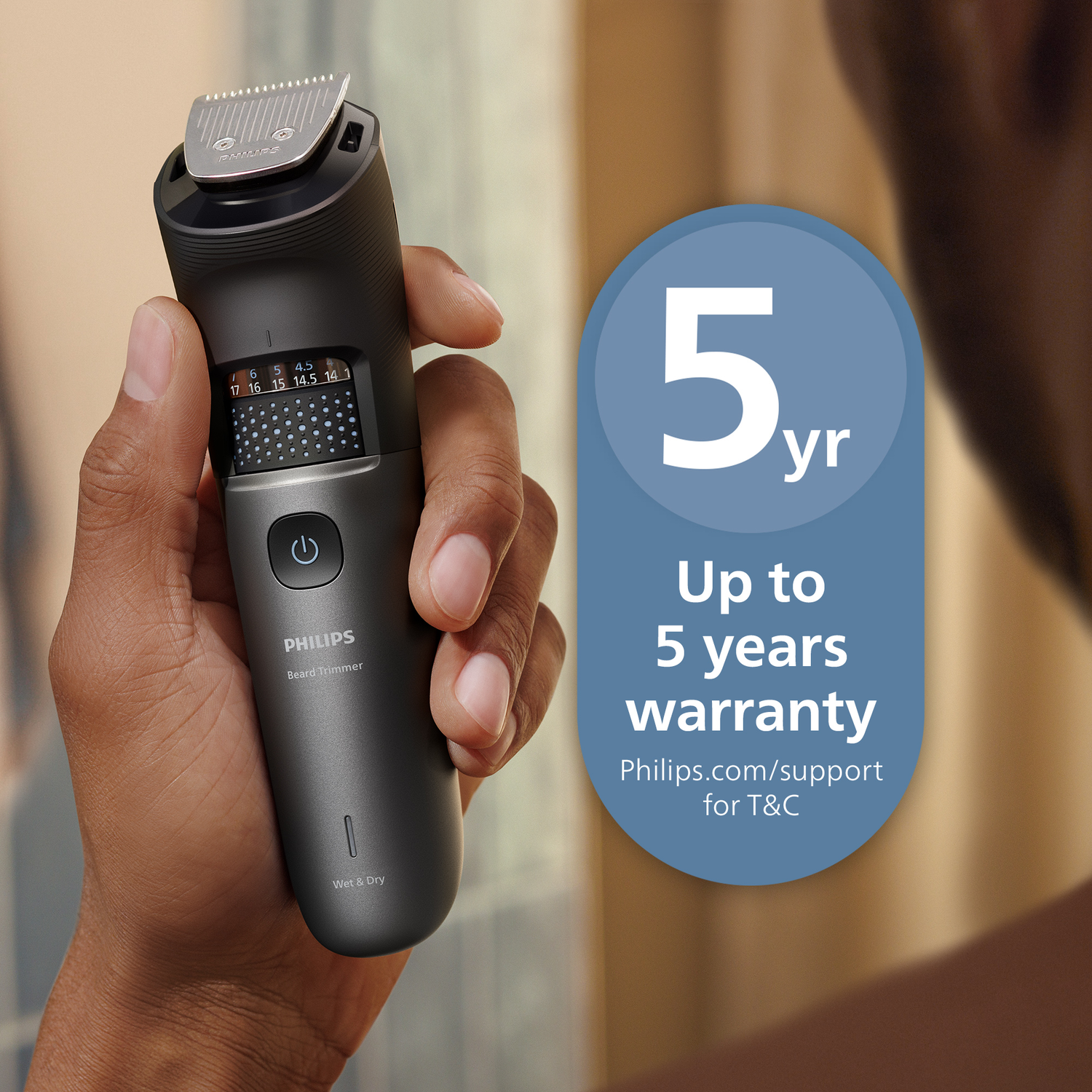 A person holds a Philips beard trimmer. The trimmer has a digital display and a power button. A blue circle highlights a 5-year warranty.