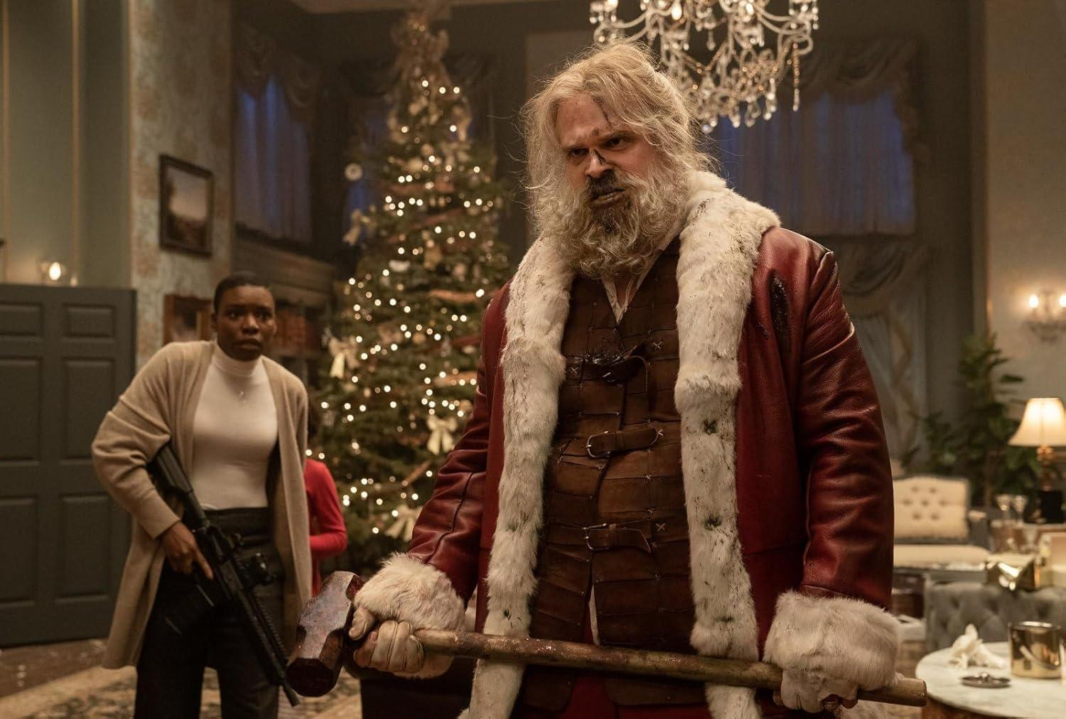 Weihnachtsmann mit Axt, Frau mit Gewehr und Weihnachtsbaum im Hintergrund. Szene ist ein dekorierter Raum.