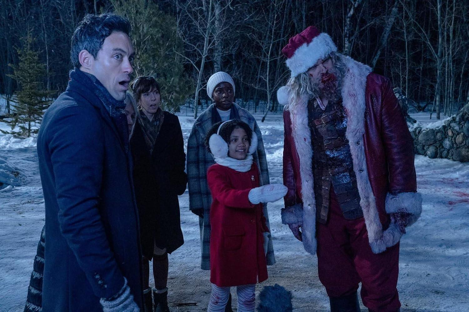 Eine Gruppe von Leuten schaut einen Zombie-Weihnachtsmann in einem verschneiten Wald an. Der Weihnachtsmann trägt einen roten Mantel und Hut mit Blut im Gesicht.