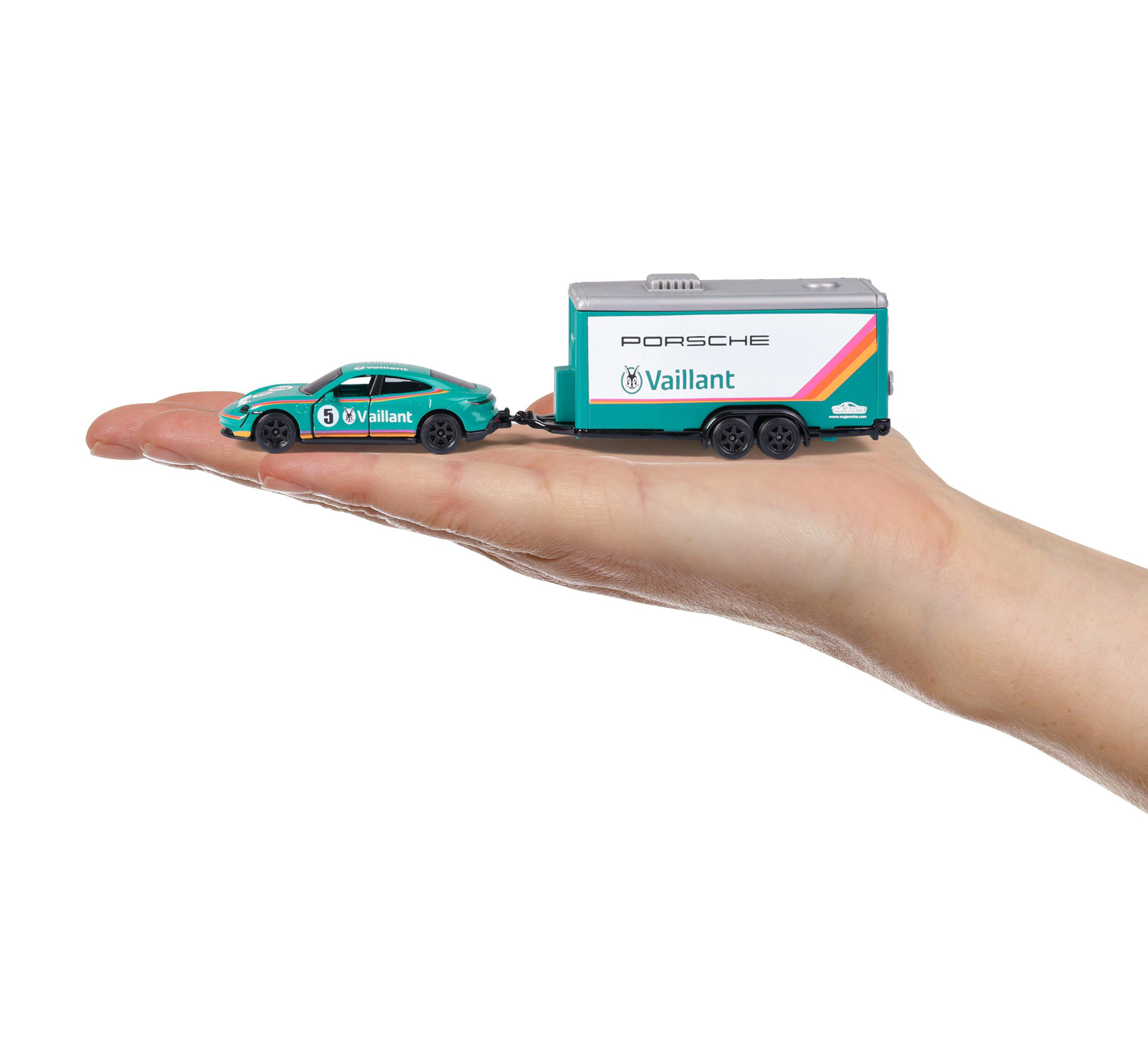 Eine Hand hält ein tealfarbenes Porsche-Spielzeugauto und einen Anhänger. Beide tragen das Vaillant-Branding. Weißer Hintergrund.