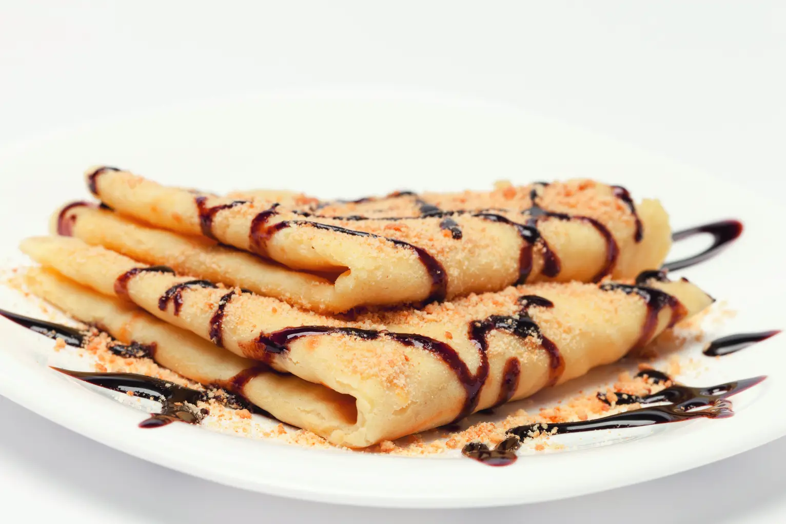 Pfannkuchen auf einem weißen Teller, mit Schokoladensauce beträufelt und mit Krümeln bestreut.