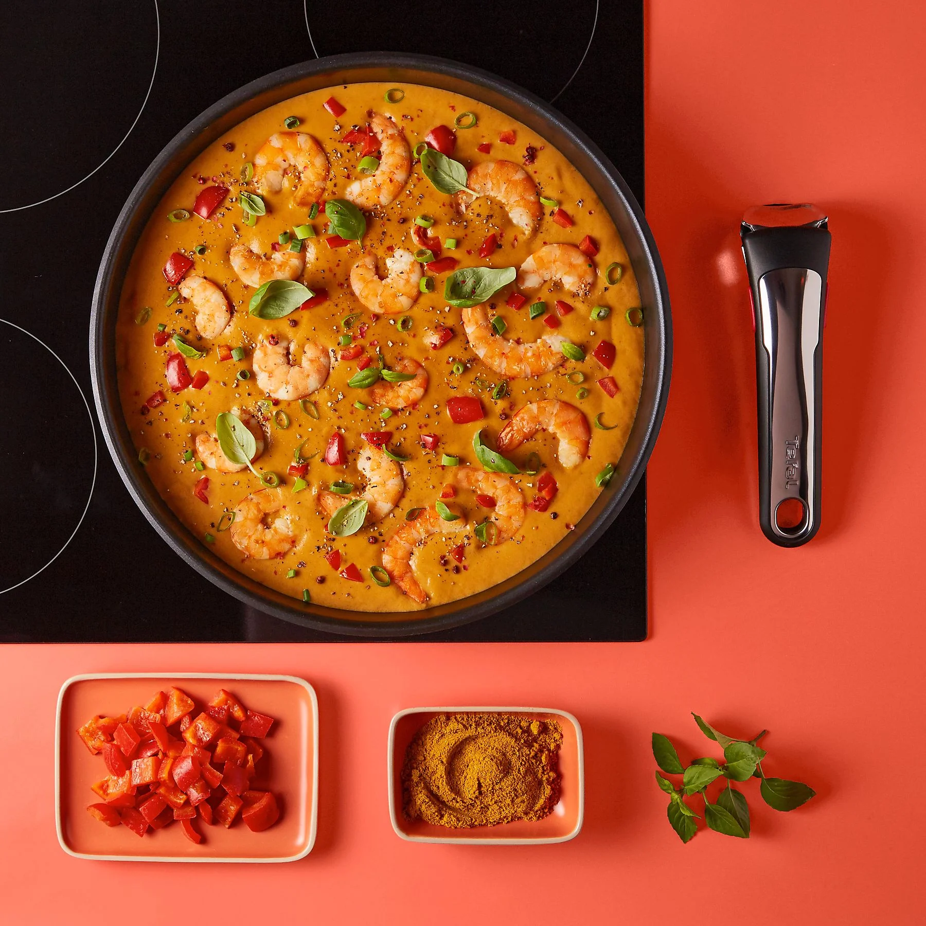 Vista dall'alto del curry di gamberi con basilico, peperoni rossi e spezie. Una padella è su un fornello. Ingredienti.
