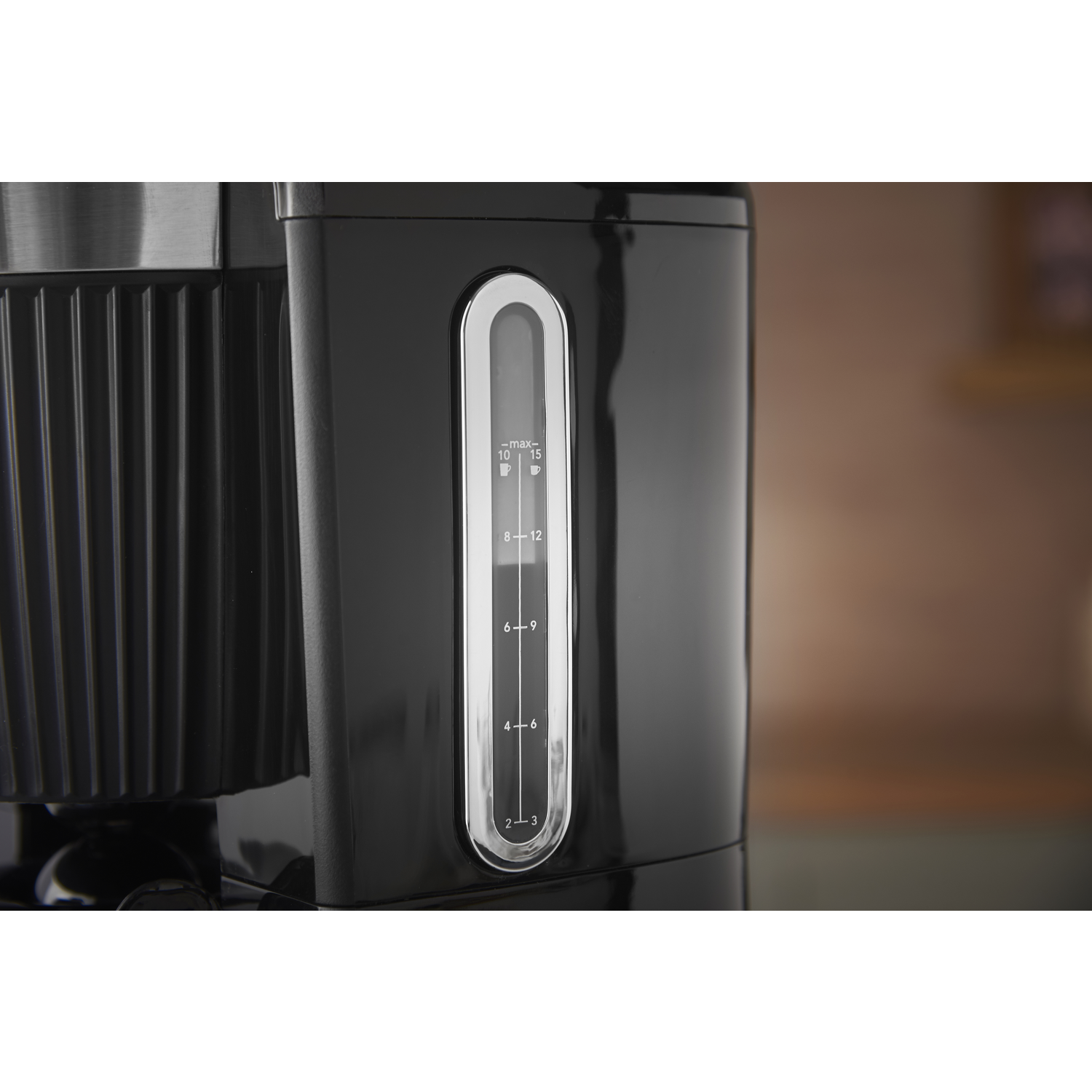 Close-up of a black coffee maker with a water level indicator. The indicator shows water levels from 2 to 12 cups. The background is blurred.