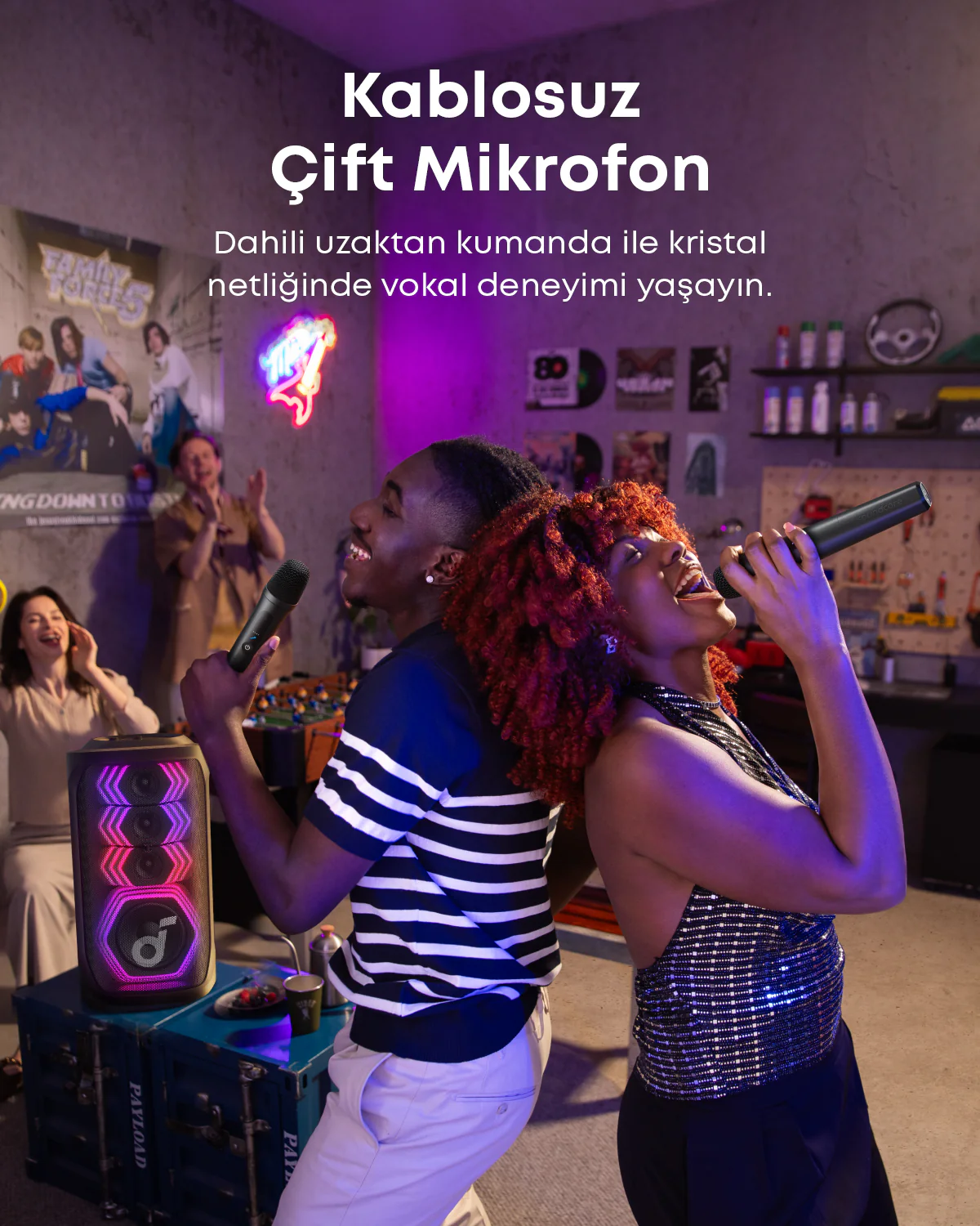 İki kişi mikrofonlara şarkı söylüyor. Arka planda renkli ışıklar ve bir poster bulunan bir hoparlör var. Sahne iç mekanda.