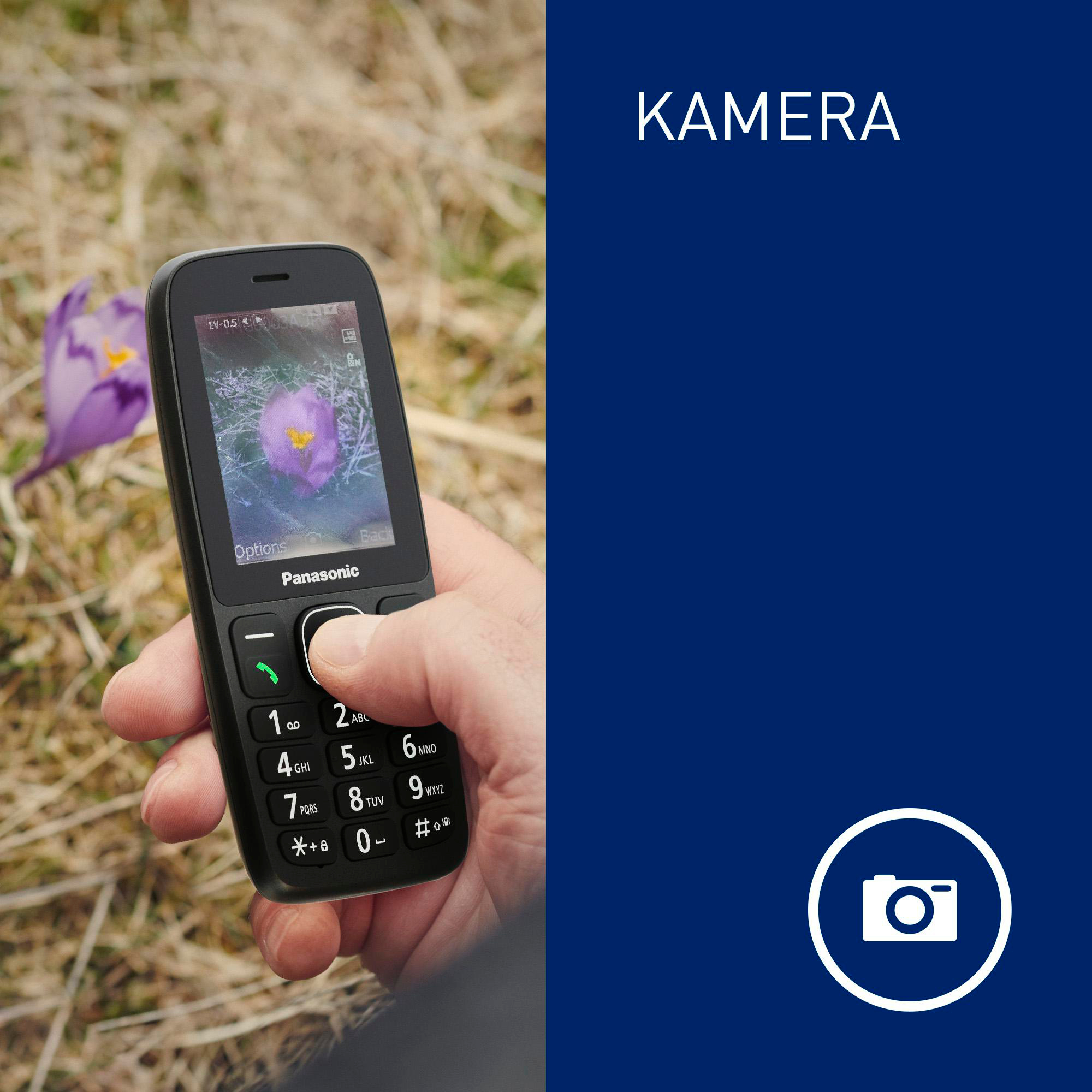Eine Hand hält ein schwarzes Panasonic-Telefon und fotografiert eine lila Krokusblume. Der Hintergrund ist blau.