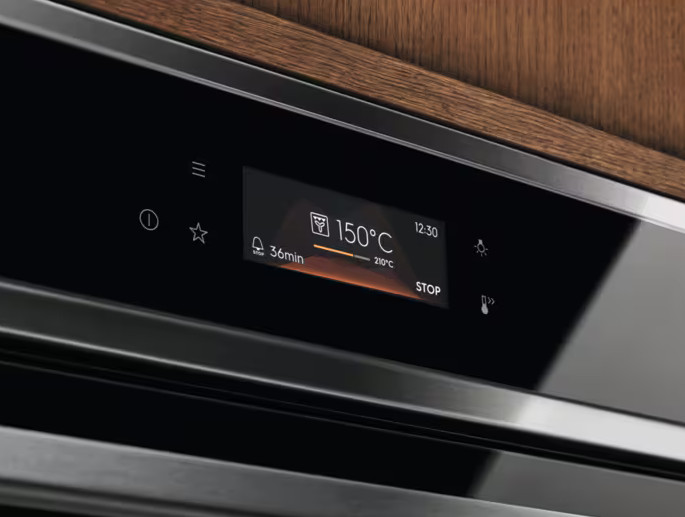 Zbliżenie panelu sterowania piekarnika wyświetlającego 150°C, 36min i 12:30. Przyciski: czas, gwiazda, dzwonek, światło i stop.