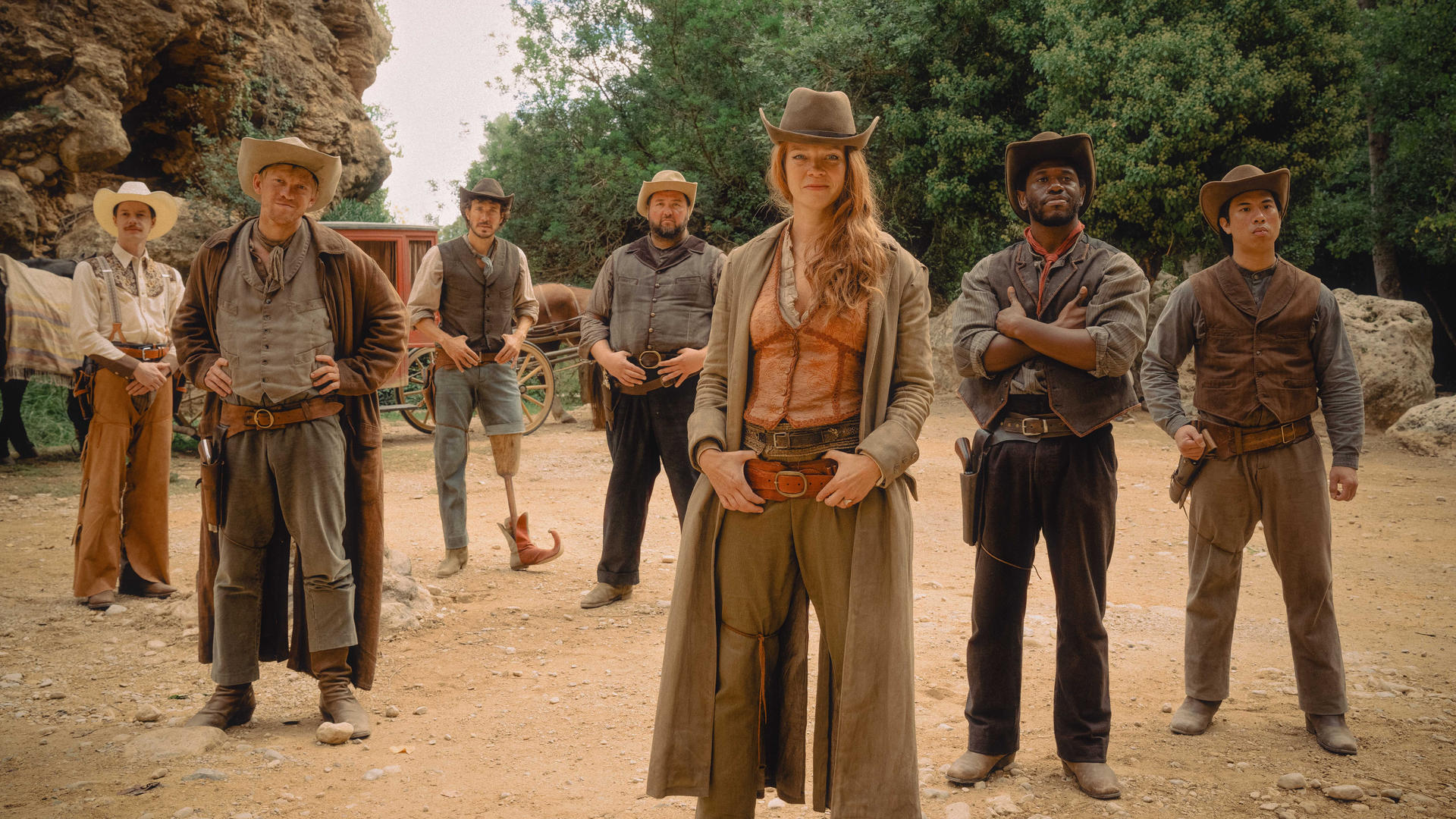 Eine Gruppe von Cowboys und Cowgirls posiert im Freien. Sie sind in Westernkleidung gekleidet. Im Hintergrund steht eine Postkutsche.