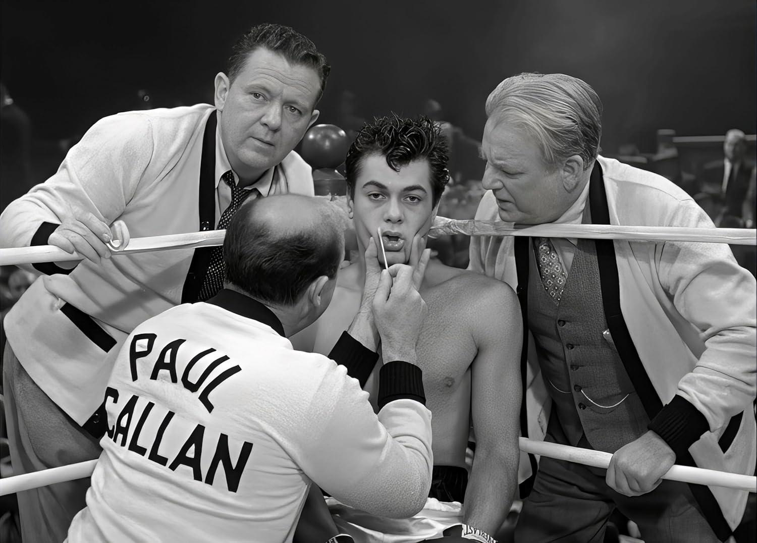 Boxer im Ring wird von seinem Team untersucht. Drei Männer in Anzügen stehen um ihn herum, einer reinigt seinen Mund mit einem Tupfer.