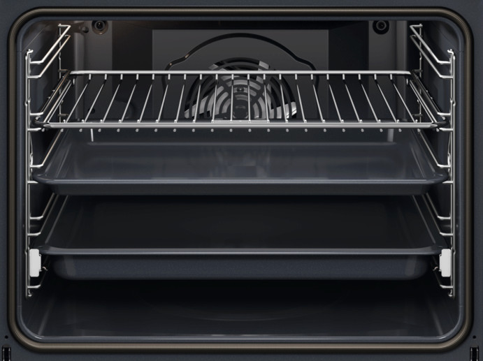 Wnętrze piekarnika. Widoczne są trzy tace. Górna to ruszt. Z tyłu znajduje się wentylator. Wnętrze jest ciemnoszare.