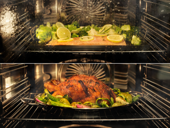 Wnętrze piekarnika z dwoma poziomami. U góry: ryba z cytryną i brokułami. Na dole: pieczony kurczak z warzywami na tacy.