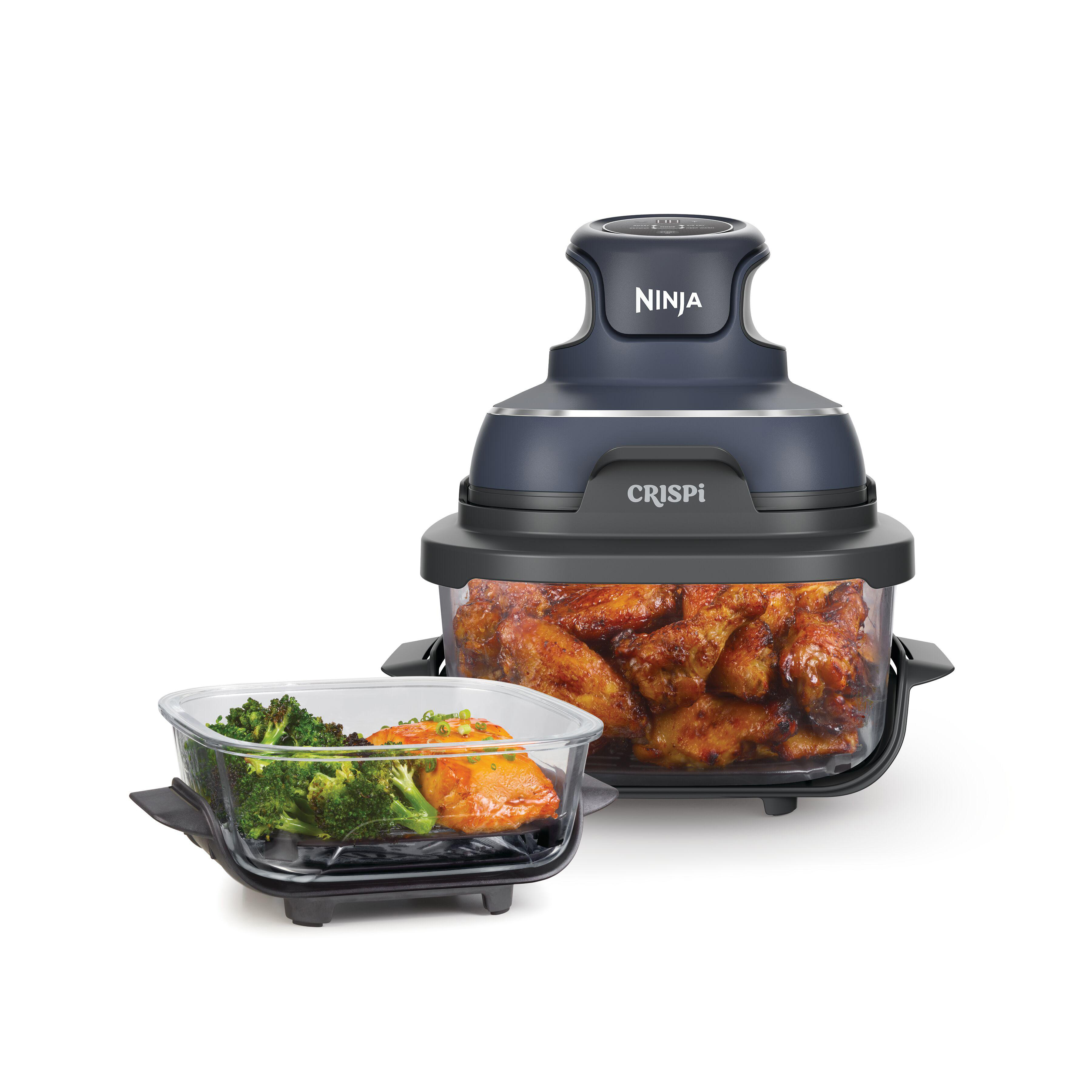 Ein Airfryer mit Hähnchenflügeln und Gemüse in Glasbehältern. Der Airfryer der Marke Ninja ist dunkelgrau.