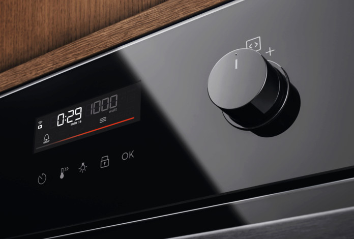 Zbliżenie czarnego panelu sterowania piekarnikiem. Posiada cyfrowy wyświetlacz pokazujący czas i moc. Po prawej stronie znajduje się duże pokrętło.
