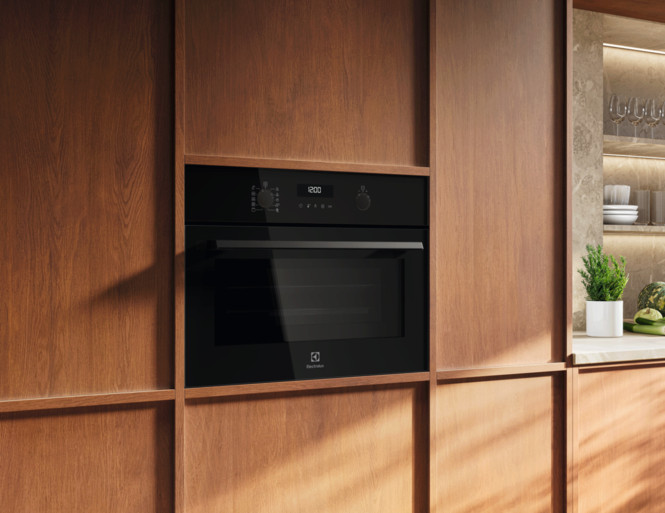 Czarny piekarnik do zabudowy z cyfrowym wyświetlaczem jest osadzony w drewnianych szafkach. W pobliżu na blacie stoi mała roślina.