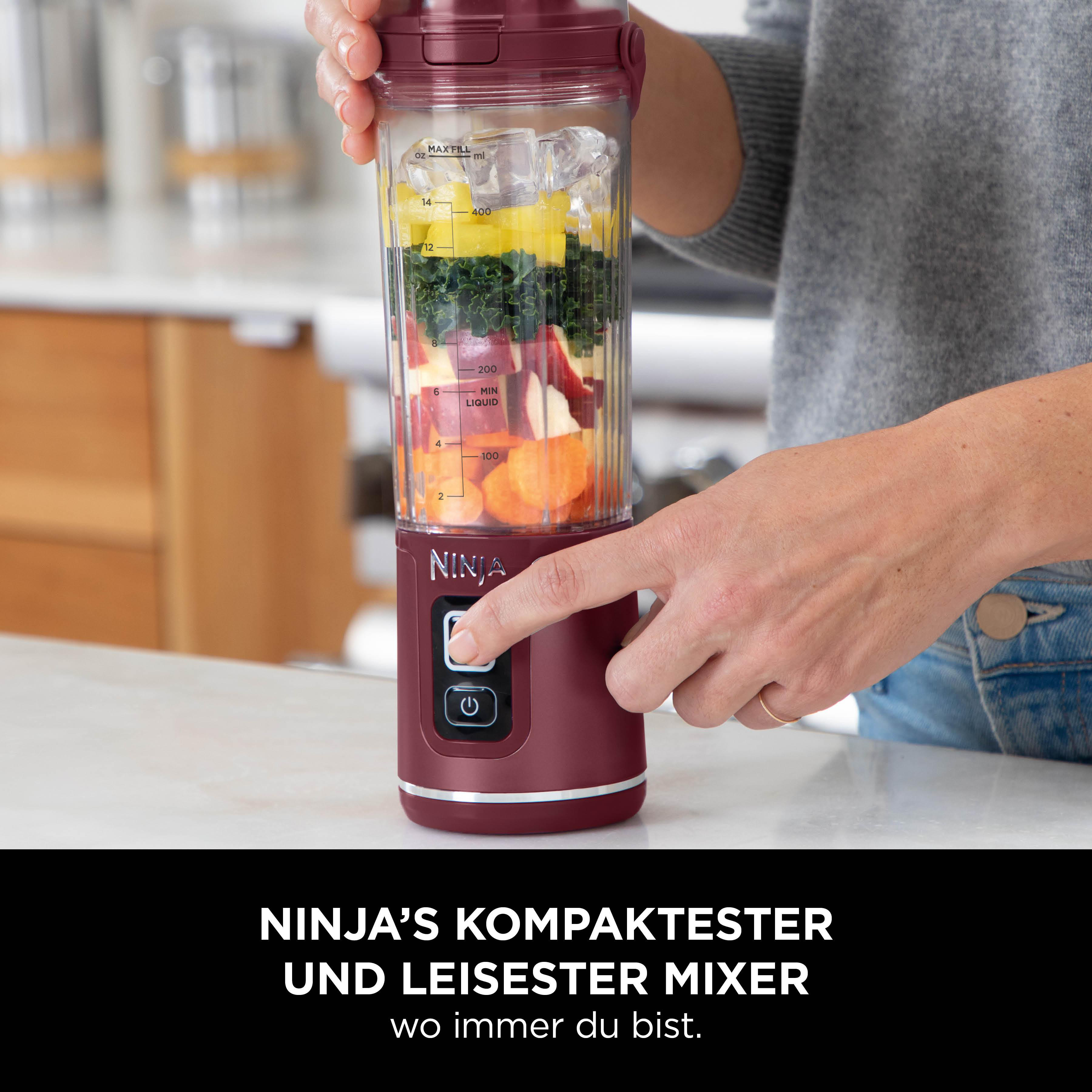Eine Frau drückt die Taste eines Ninja-Mixers. Der Mixer enthält Eis, Früchte und Gemüse. Der Text lautet: Ninja's kompakter Mixer.