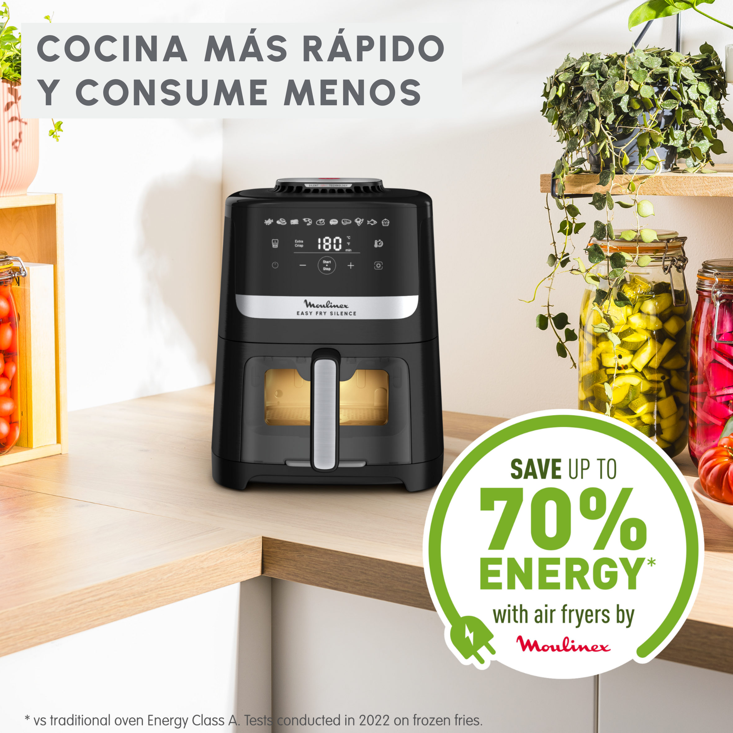 Una freidora de aire negra con pantalla digital está sobre una encimera. Tarros de comida y plantas al fondo. Texto: Ahorra hasta un 70% de energía.
