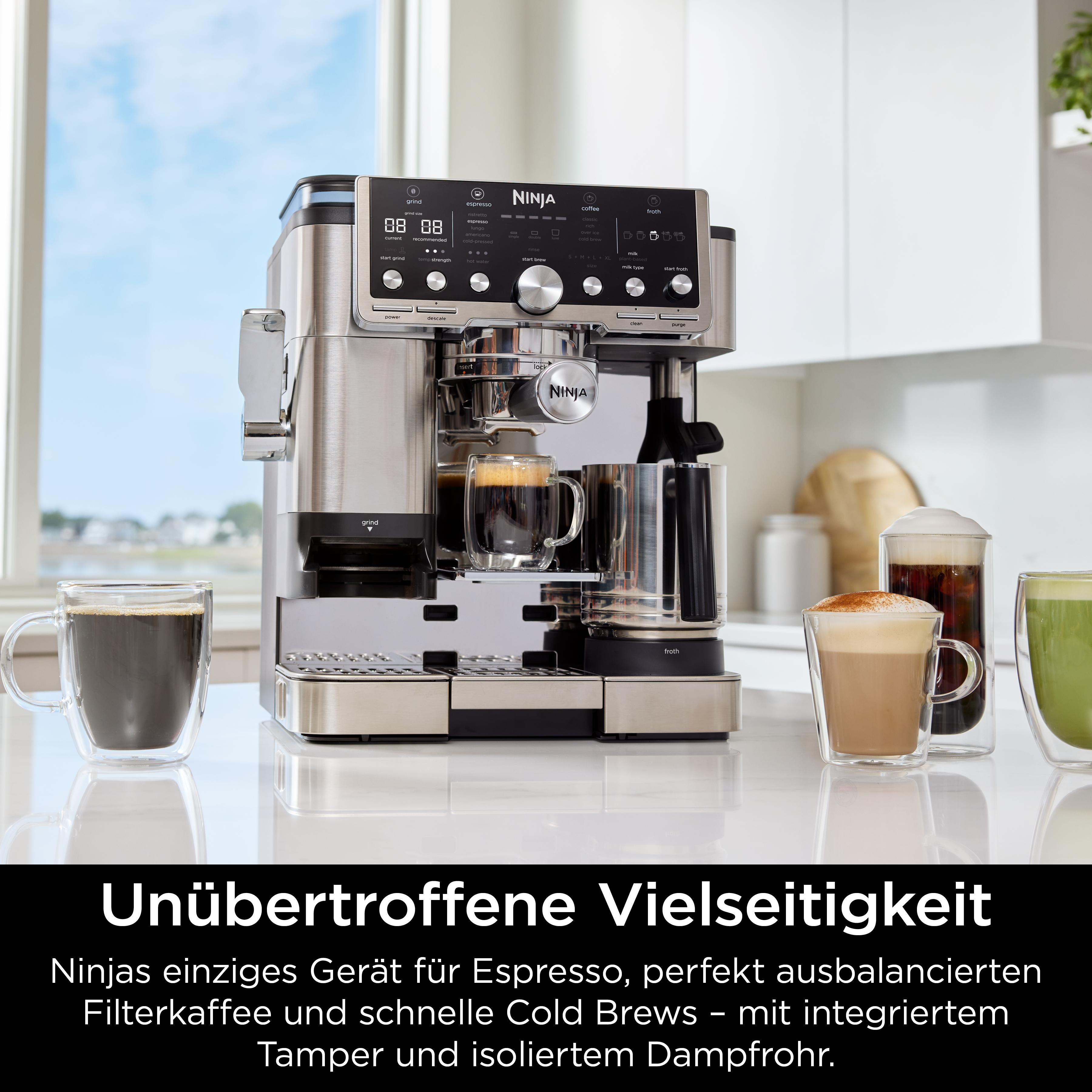 Eine silberne Ninja-Kaffeemaschine mit Kaffeetassen steht auf einer weißen Oberfläche. Fenster im Hintergrund.