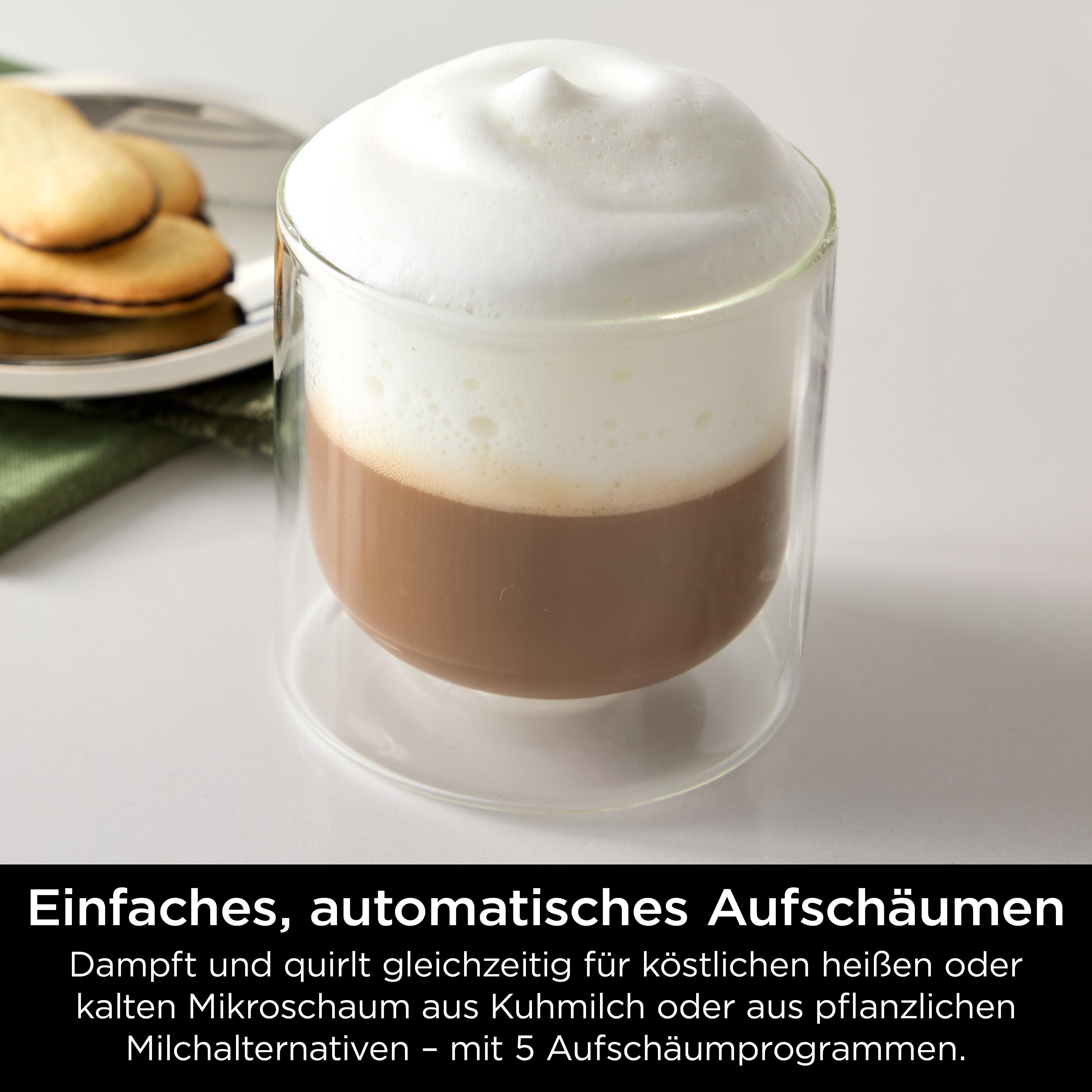 Ein Glas Cappuccino mit einer dicken Schicht weißen Schaums. Daneben liegt ein Teller mit Keksen auf einem grünen Tuch.