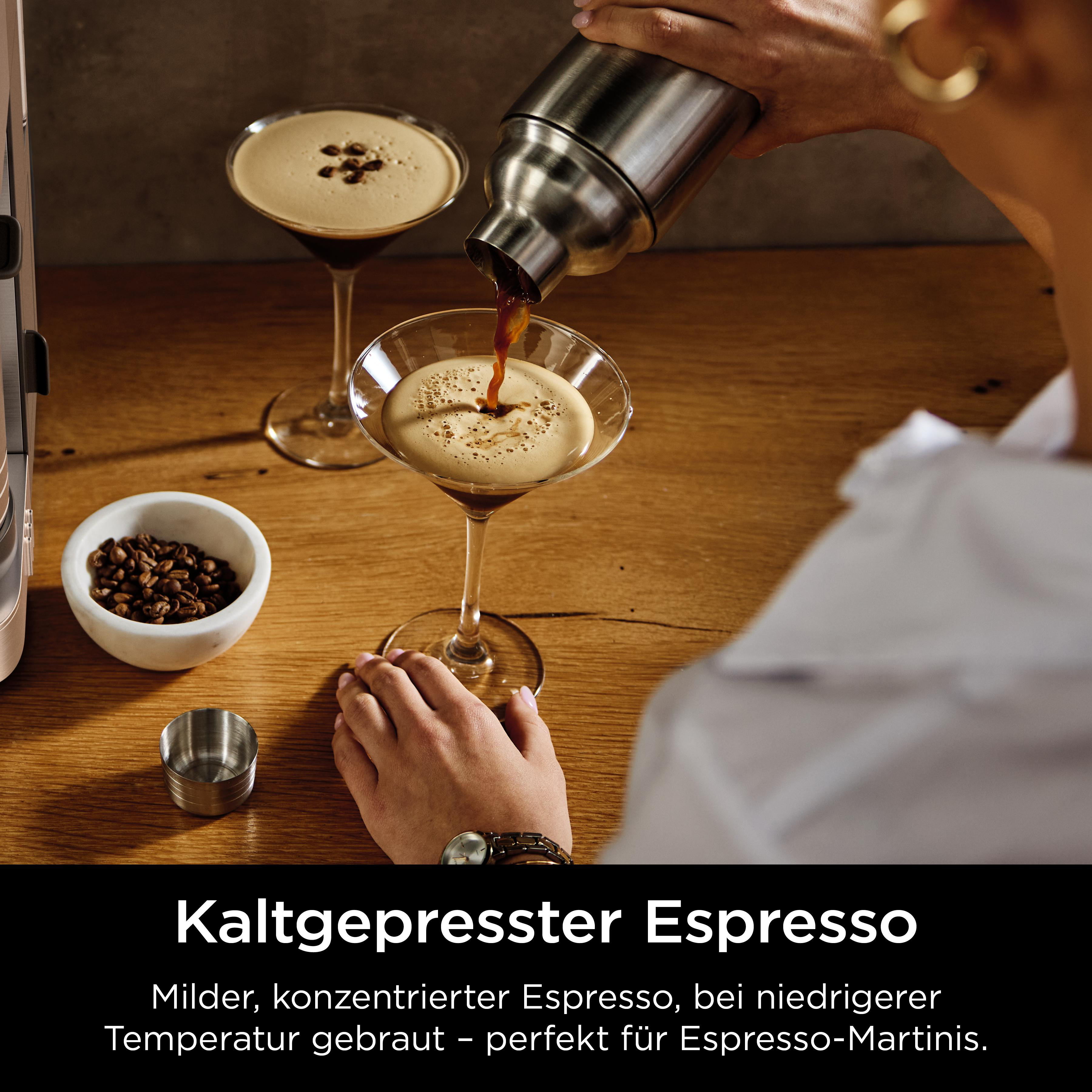 Eine Person gießt Espresso in ein Martini-Glas. Kaffeebohnen und ein Messbecher liegen auf Holz.