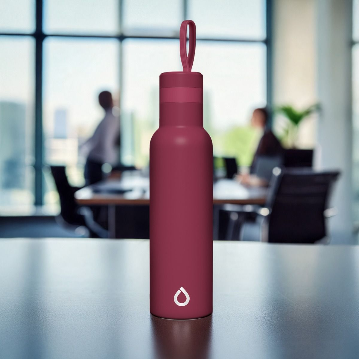 Bordowa butelka na wodę z uchwytem w kształcie pętli stoi na stole. W rozmytym tle trwa spotkanie.