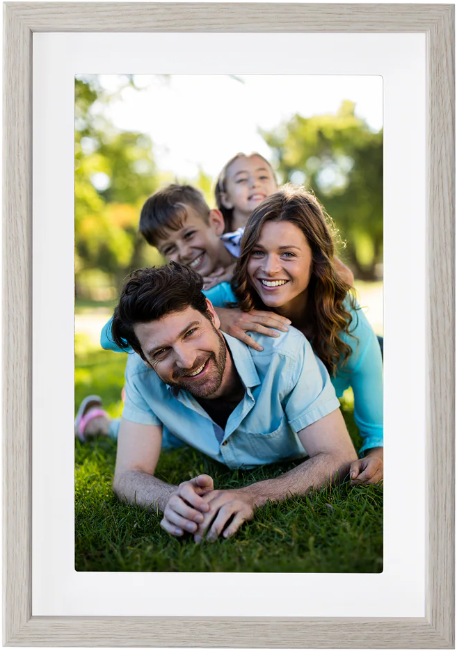 Une famille sourit sur l'herbe. Un homme est allongé, une femme et deux enfants sont derrière lui. L'arrière-plan est un parc.