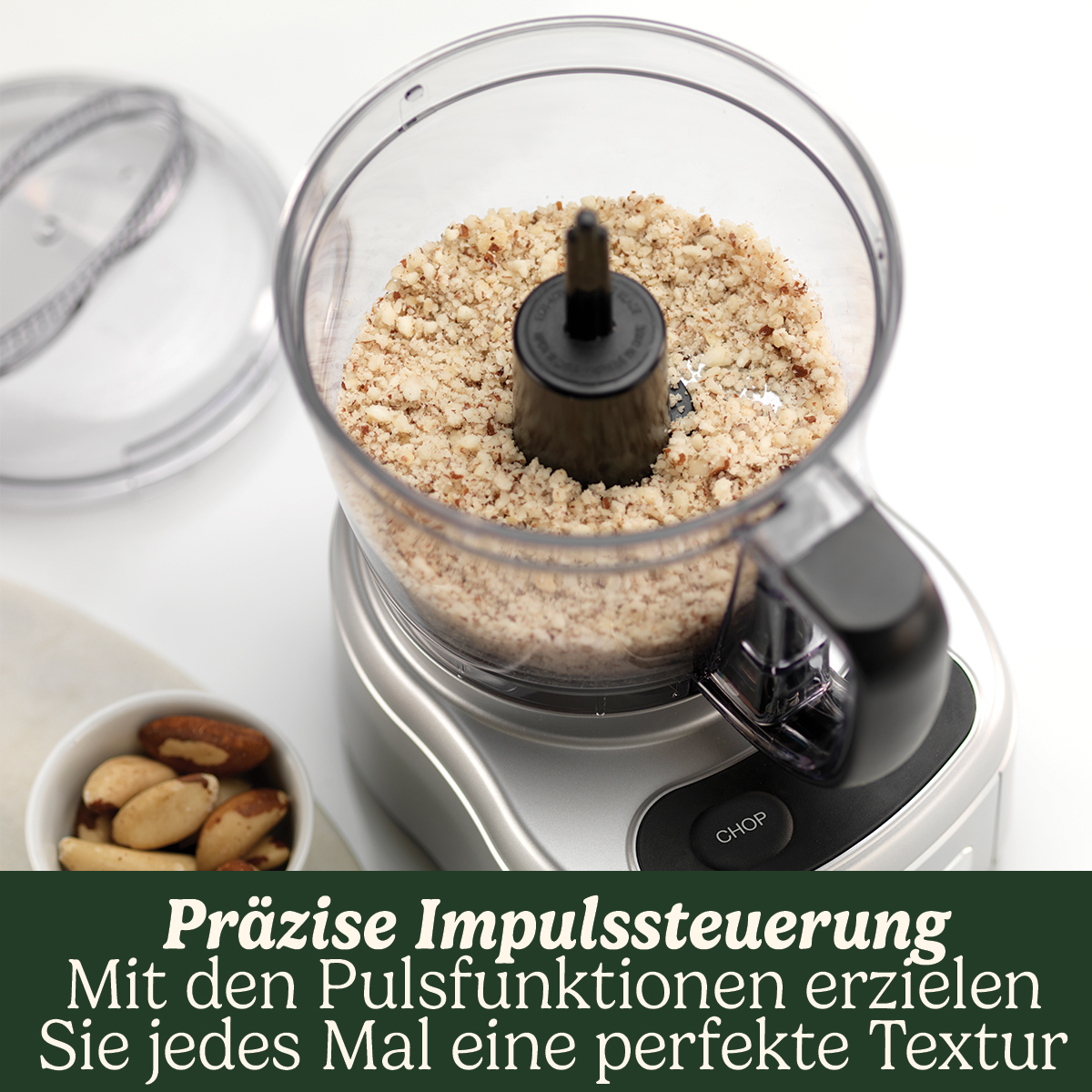 Küchenmaschine mit gehackten Nüssen. Paranüsse in einer kleinen Schüssel im Vordergrund. Das Gerät steht auf weißer Oberfläche.