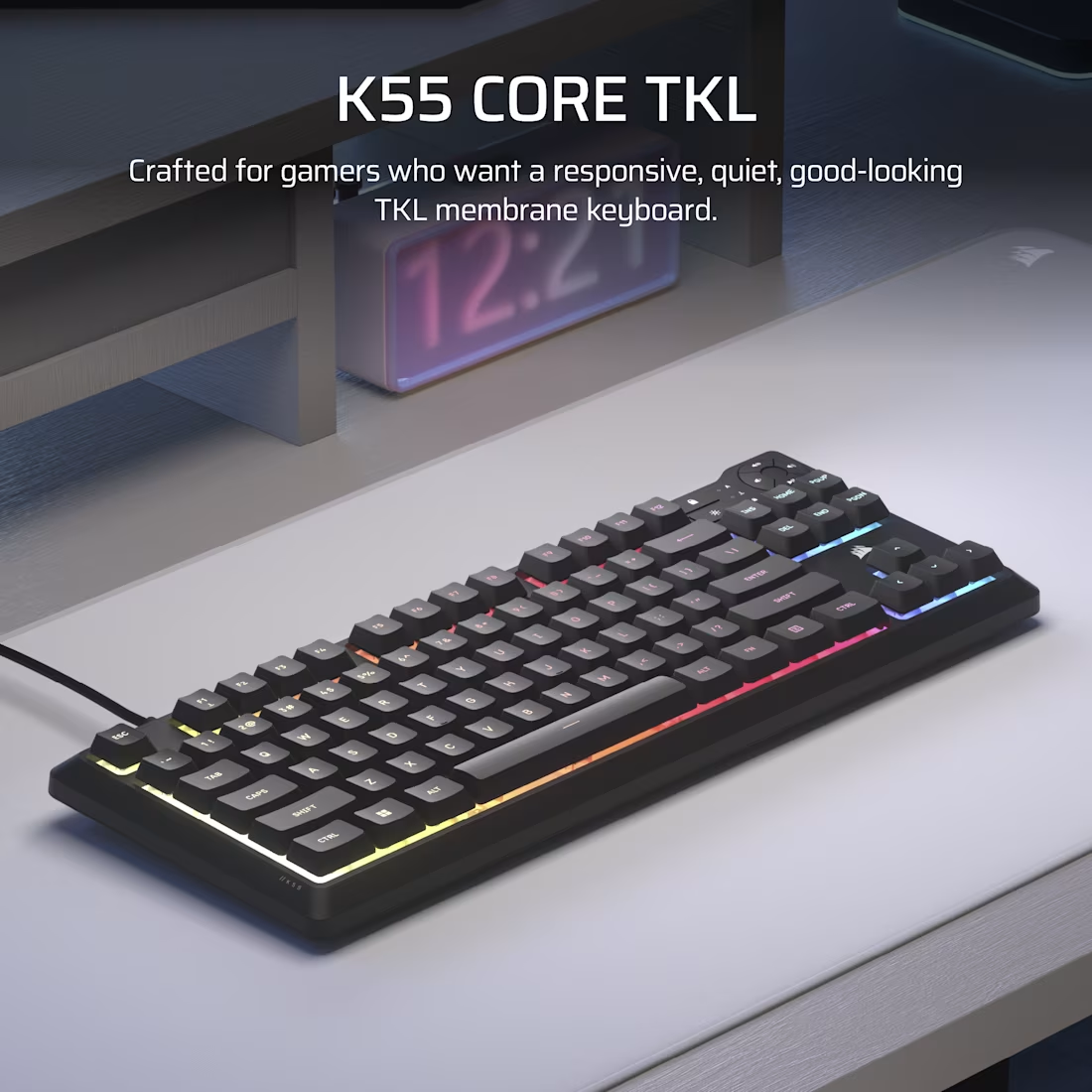 Clavier noir K55 Core TKL sur une surface blanche. Touches éclairées aux couleurs de l'arc-en-ciel. Une horloge numérique et un bureau sont visibles.