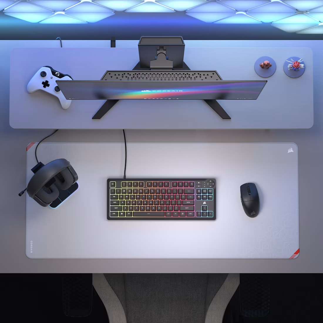 Vue de dessus d'une configuration de jeu. Comprend un moniteur, un clavier, une souris, une manette, un casque et des éléments décoratifs sur un bureau blanc.