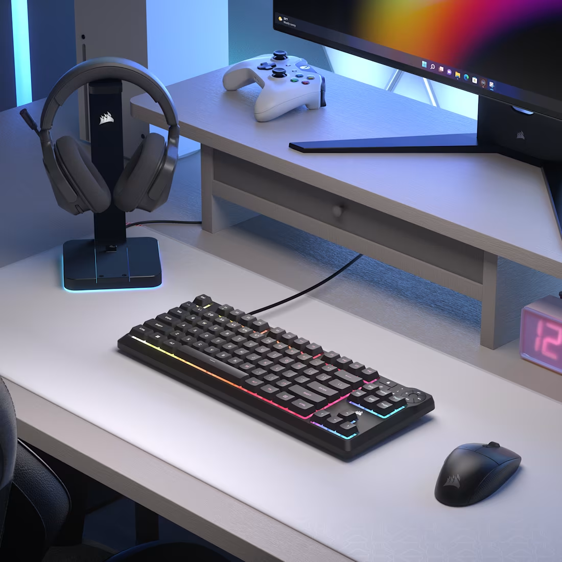 Une configuration de jeu avec clavier RGB, souris, casque et moniteur. Une manette est sur un bureau.