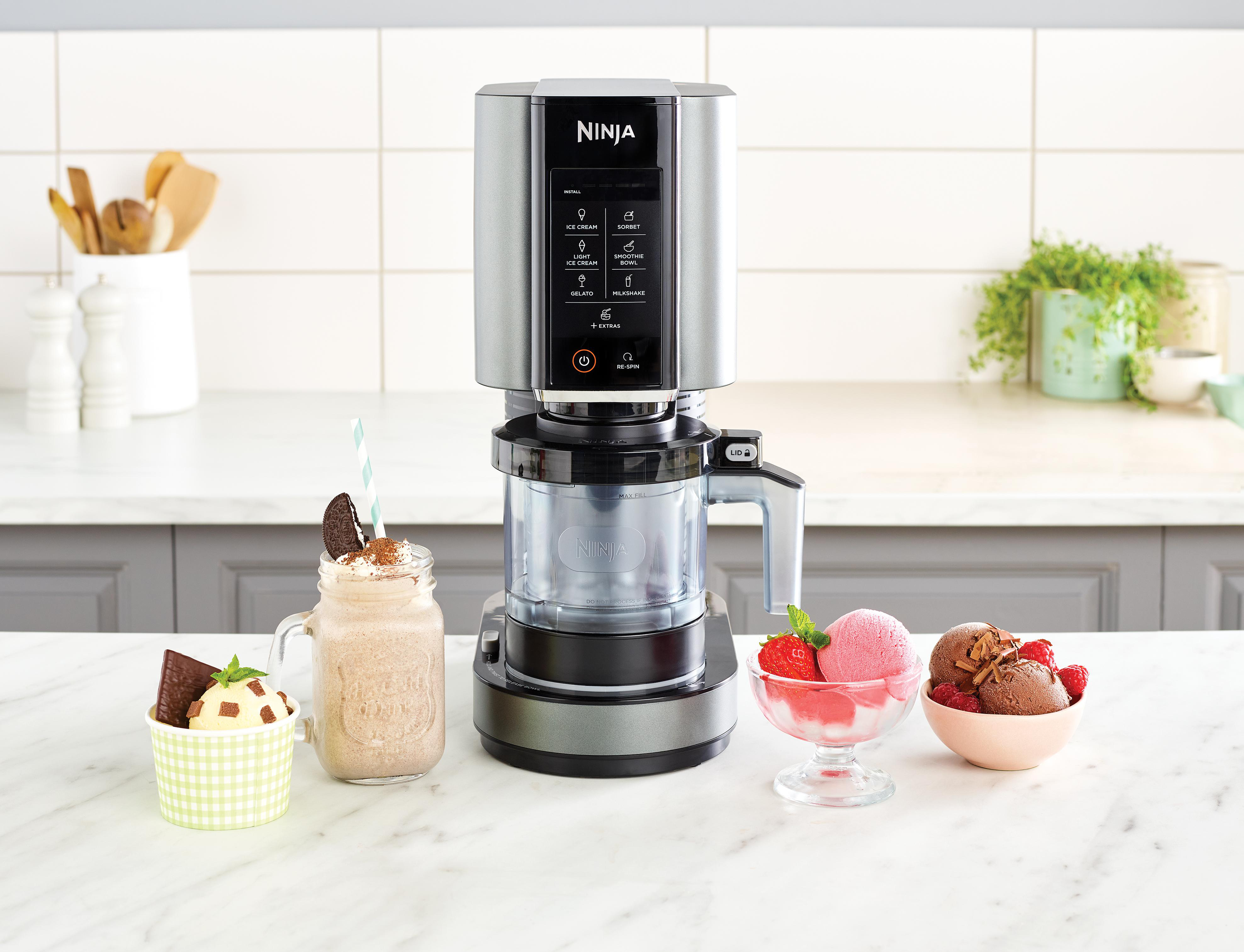 Eine Eismaschine mit Eis- und Milchshake-Proben. Der Hintergrund zeigt eine Küche mit Pflanzen und Utensilien.