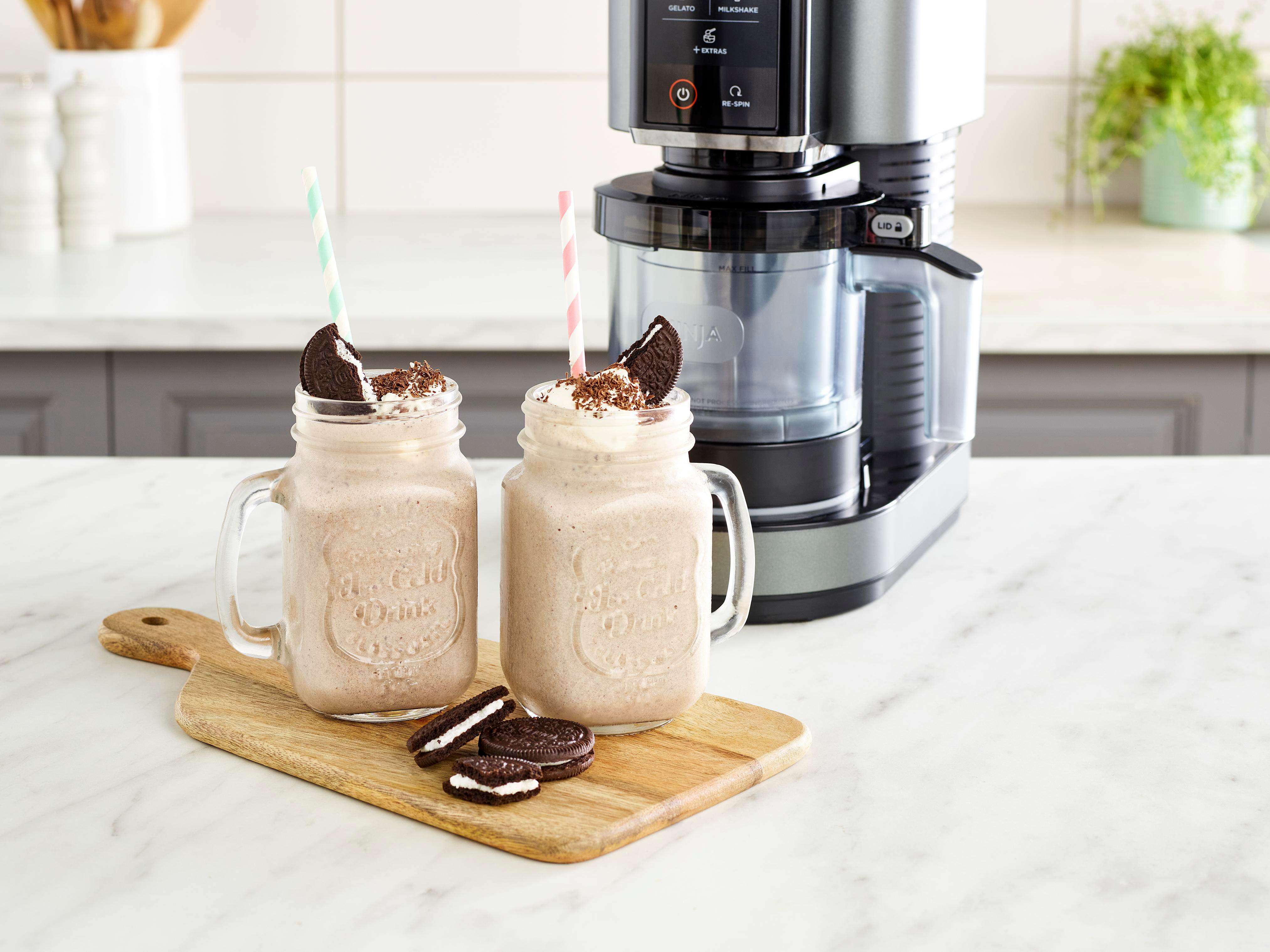 Zwei Milchshakes in Gläsern mit Strohhalmen und Oreo-Keksen. Ein Mixer steht dahinter auf einer Marmoroberfläche.